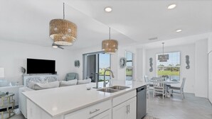 A modern kitchen with a central island, white cabinetry, and a large window offering a view of the outdoors.