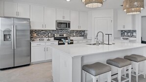 A modern kitchen with white cabinetry, stainless steel appliances, a central island with bar stools, and decorative woven light fixtures.