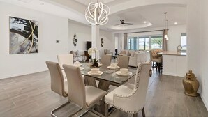 Een moderne eetruimte met een glazen tafel, beige gestoffeerde stoelen en een unieke hanglamp.