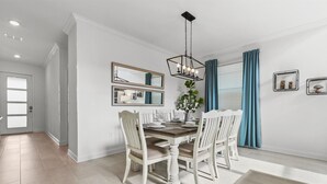 Een eetgedeelte met een houten tafel, witte stoelen en een hanglamp.