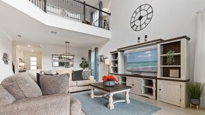 Een ruime woonkamer met een hoge plafond, een grote flatscreen televisie en een balkon.