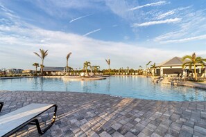 A large outdoor swimming pool with lounge chairs and palm trees, surrounded by buildings.