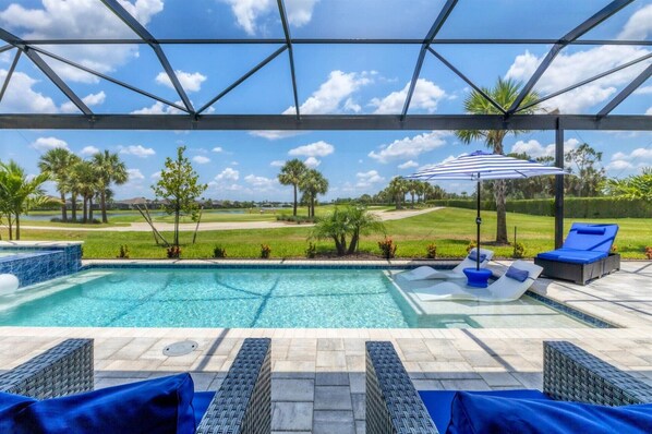 A swimming pool with lounge chairs and an umbrella, surrounded by a covered patio area with a view of a golf course.