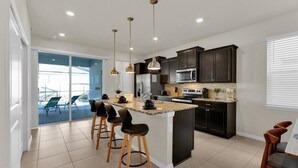 A modern kitchen with a central island, dark cabinetry, stainless steel appliances, and pendant lighting. - Orlando Villa 6462: Private Pool & Resort Amenities (Orlando)