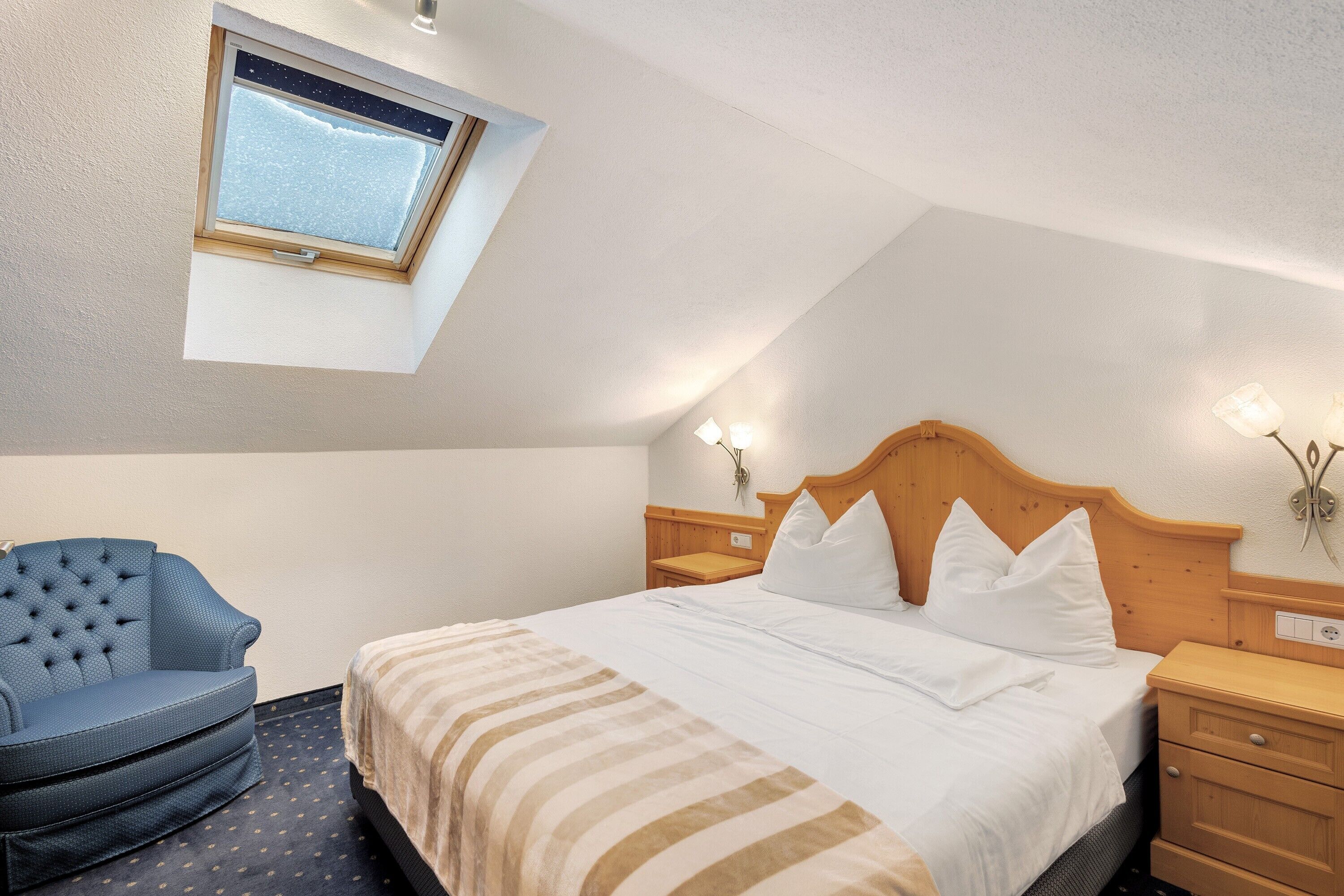A bedroom with a bed, a chair, a nightstand, a lamp, and a window.