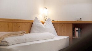 Un llit ben fet amb llençols blancs, una làmpada de nit i un panell de fusta al capçal.