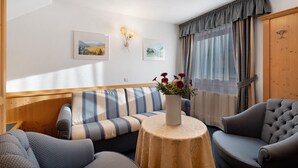Habitació amb un sofà, butaques, una taula rodona amb un vas i dues làmpades penjades a la paret.
