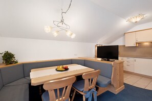 A modern kitchen with a built-in oven, a dining area with a wooden table and blue upholstered chairs, and a TV mounted on the wall. - Apartment 'Loderhof Sternenhimmel' with Mountain View, Shared Garden and Wi-Fi (Sand in Taufers)