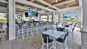 Ein Außenbereich zum Essen mit mehreren Tischen und Stühlen, eine Bar mit Fernseher und Blick auf den Pool.