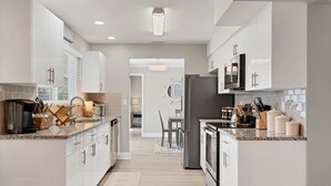 A modern kitchen with white cabinetry, granite countertops, and stainless steel appliances.