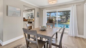 A dining area with a wooden table and chairs, a bowl on the table, and a view of a swimming pool through large windows.