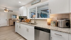 A modern kitchen with white cabinetry, a granite countertop, a dishwasher, and a window with blinds.