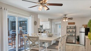 A modern kitchen with white cabinets, a dining area with white chairs, and a ceiling fan.