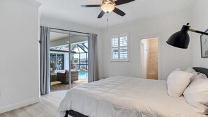 Een slaapkamer met een bed, een plafondventilator, een raam en een deur die uitkomt op een balkon.