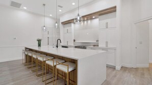Een moderne keuken met een groot eiland, barstoelen, hangende verlichting en witte kasten.
