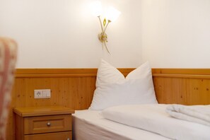 A hotel room with a wooden headboard, a bedside table with drawers, a wall-mounted light fixture, and a white bed with pillows. - Apartment 'Loderhof Blumenwiese' with Mountain View, Shared Garden & Wi-Fi (Sand in Taufers)