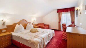 A hotel room with a wooden bed, a desk, two chairs, a red carpet, and a white ceiling light. - Apartment 'Loderhof Blumenwiese' with Mountain View, Shared Garden & Wi-Fi (Sand in Taufers)