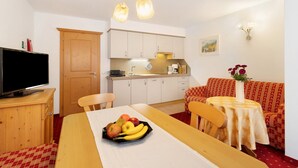 A room with a bed, a TV, a dining table with fruit, a sofa, and a kitchen area. - Apartment 'Loderhof Blumenwiese' with Mountain View, Shared Garden & Wi-Fi (Sand in Taufers)