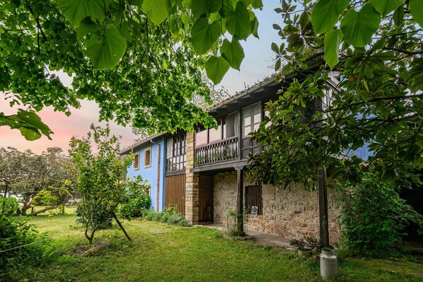 A two-story house with a stone facade, a balcony, and a garden.