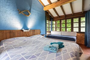 A bedroom with a large bed, a wooden headboard, a wall-mounted light fixture, and a window with curtains.