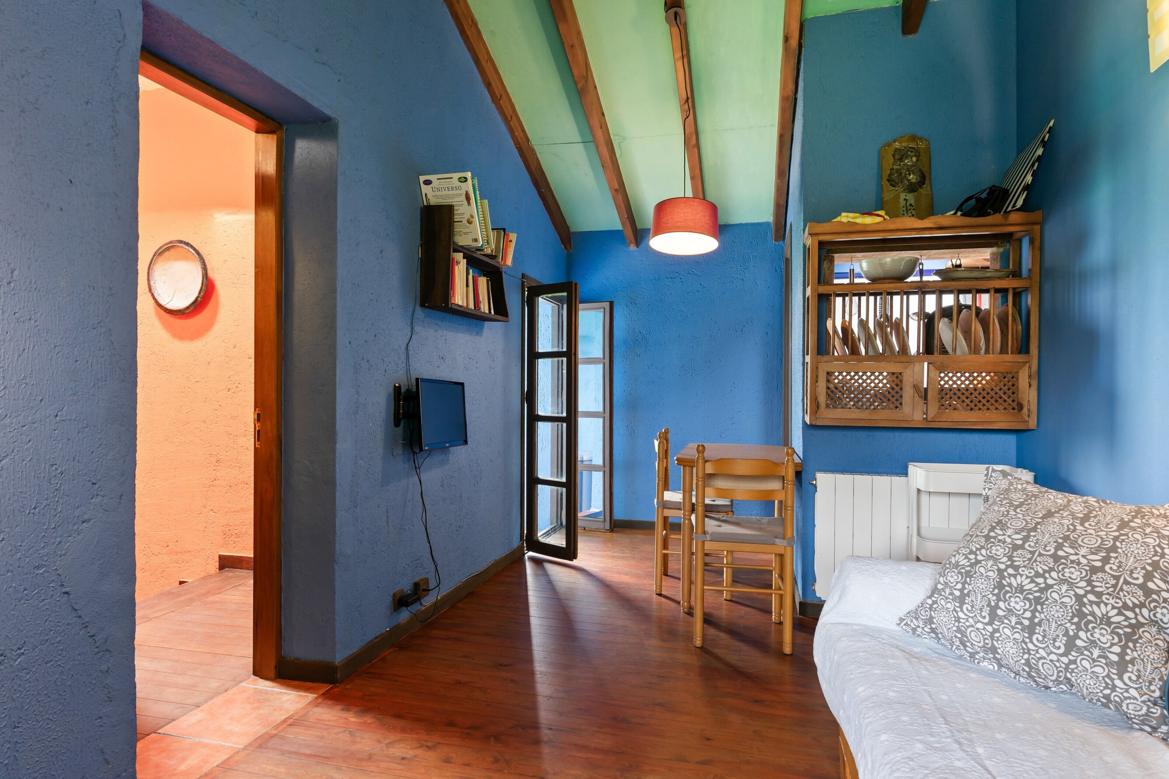 A room with a bed, wooden chairs, a bookshelf, a hanging light fixture, and a window.