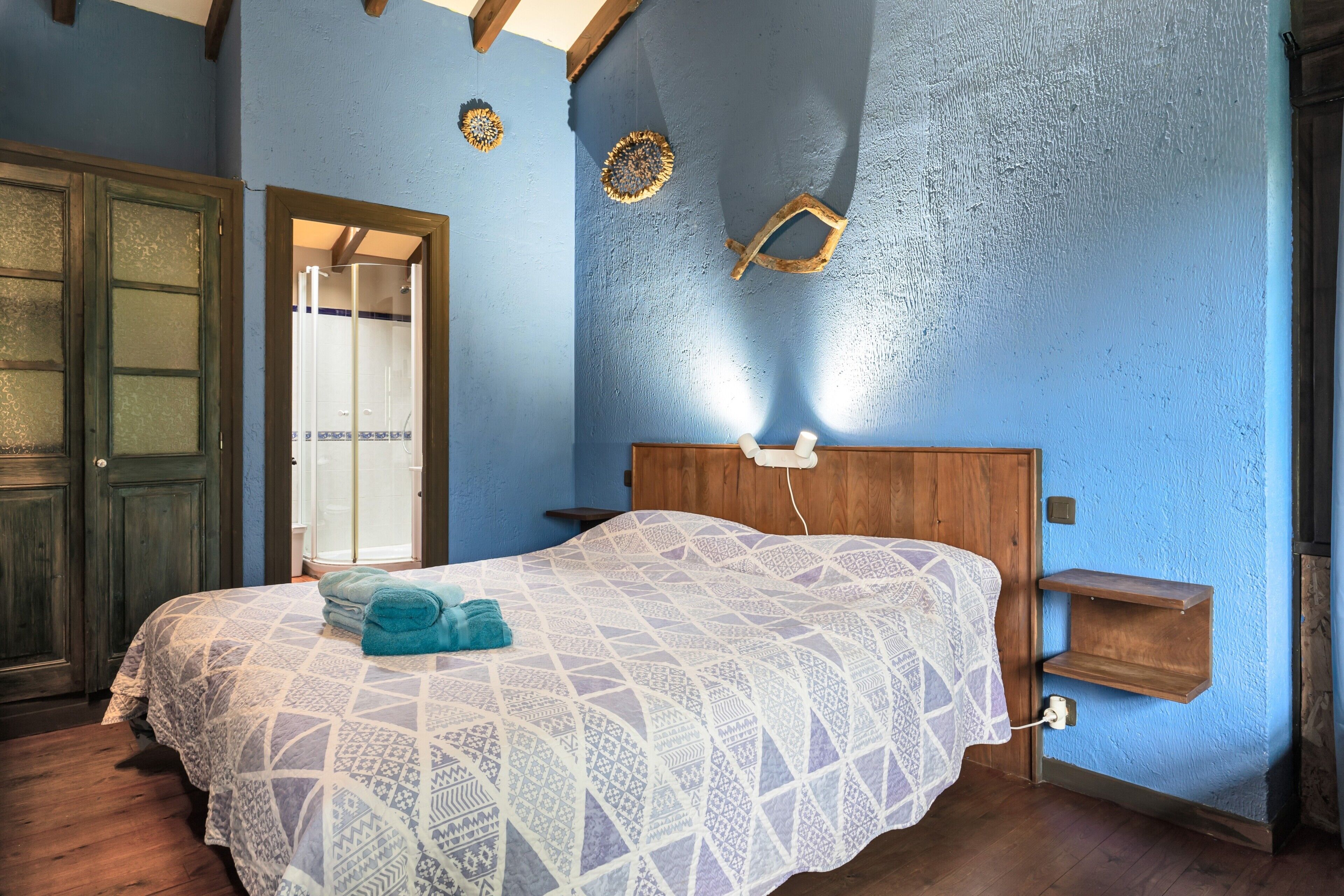 A bedroom with a wooden headboard, a patterned bedspread, a blue wall, and a wooden door.