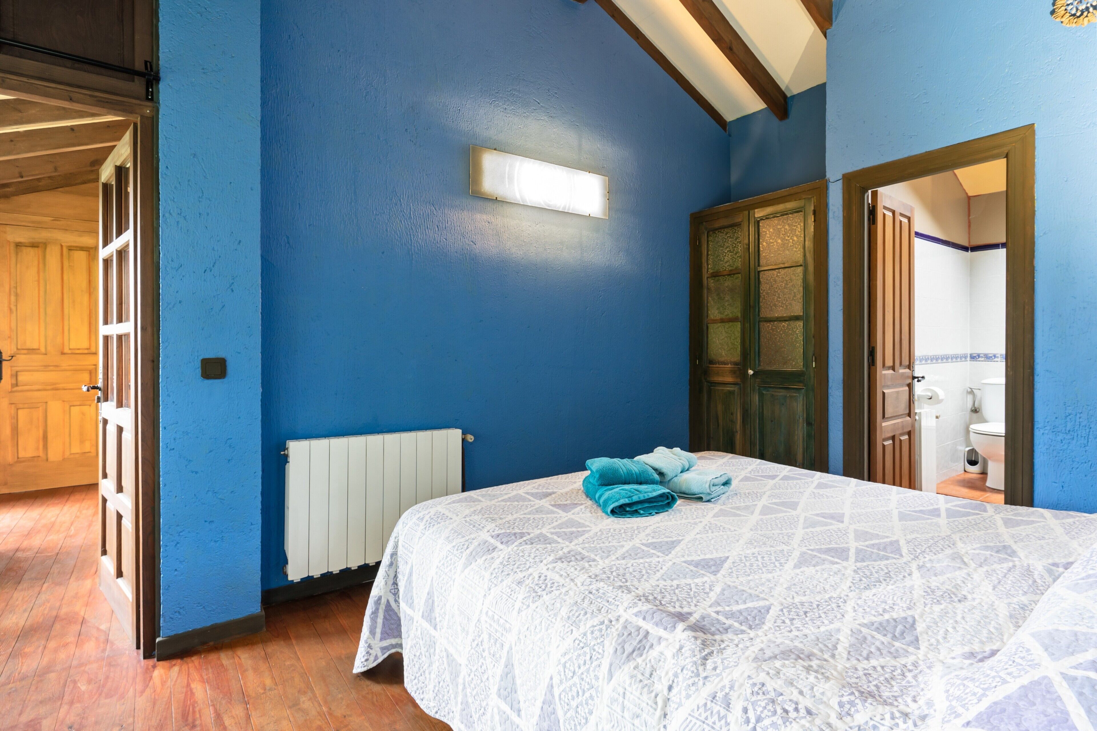 Un dormitorio con una pared azul, una cama con una colcha blanca estampada, un radiador y una puerta que da a otra habitación.