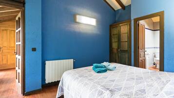 Un dormitorio con una pared azul, una cama con una colcha blanca estampada, un radiador y una puerta que da a otra habitación.