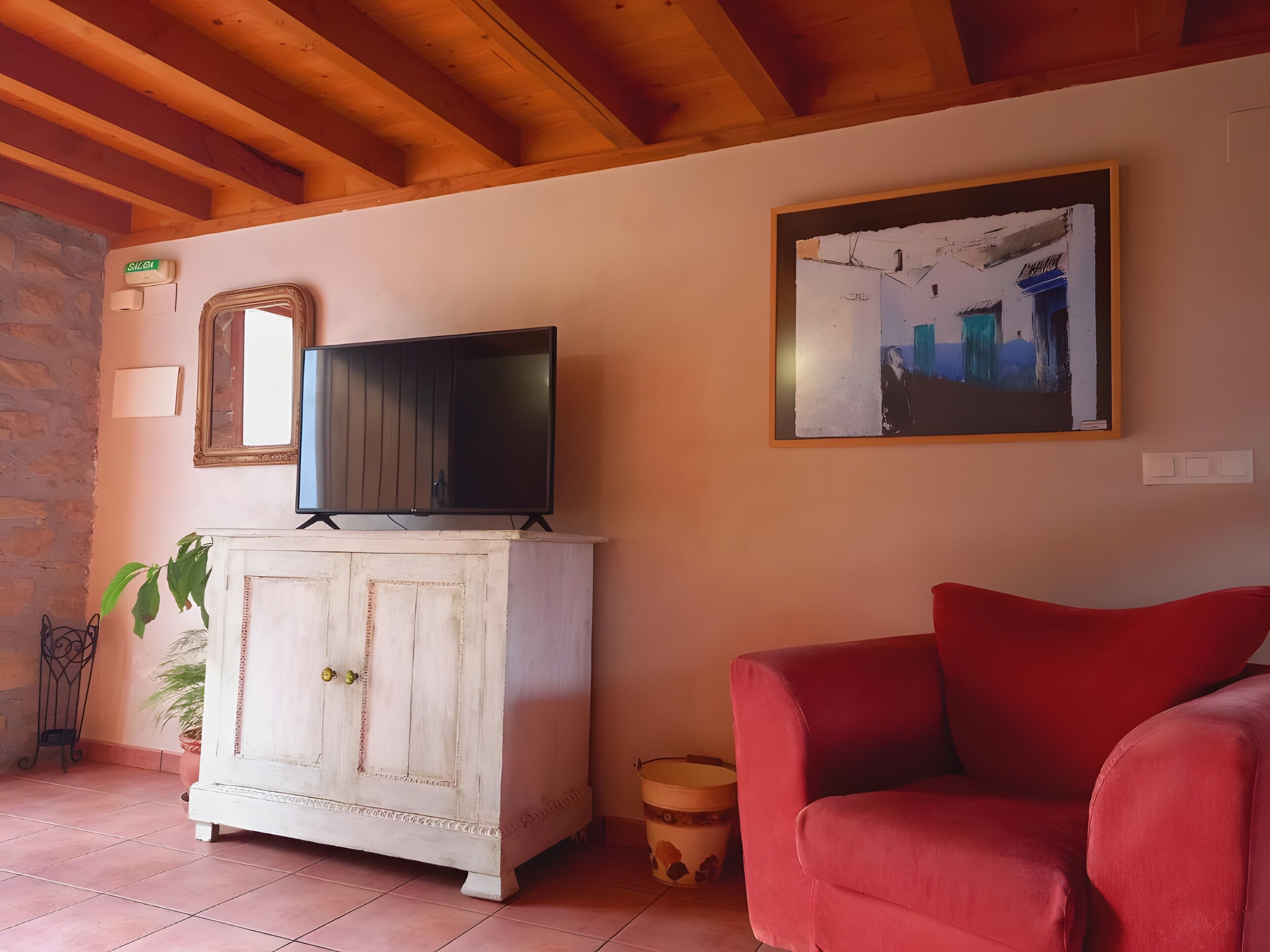 A living room with a television on a cabinet, a red sofa, a framed picture on the wall, and a potted plant.