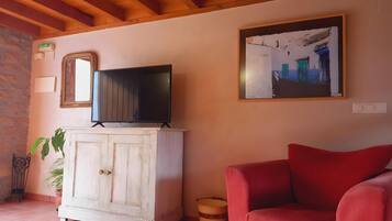 A living room with a television on a cabinet, a red sofa, a framed picture on the wall, and a potted plant.