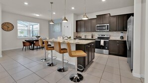 A modern kitchen with dark cabinets, stainless steel appliances, and a central island with bar stools.