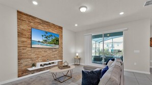 A modern living room with a wooden wall, a flat-screen TV, a sofa, and a glass door leading to a balcony.