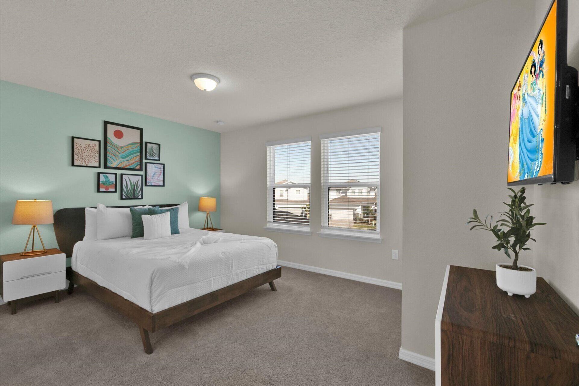 A bedroom with a bed, two bedside tables with lamps, a large window with blinds, and a wall-mounted TV.