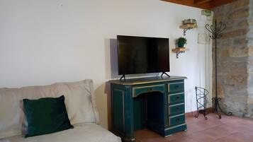 A living room with a sofa, a TV on a stand, a desk, and a stone wall.