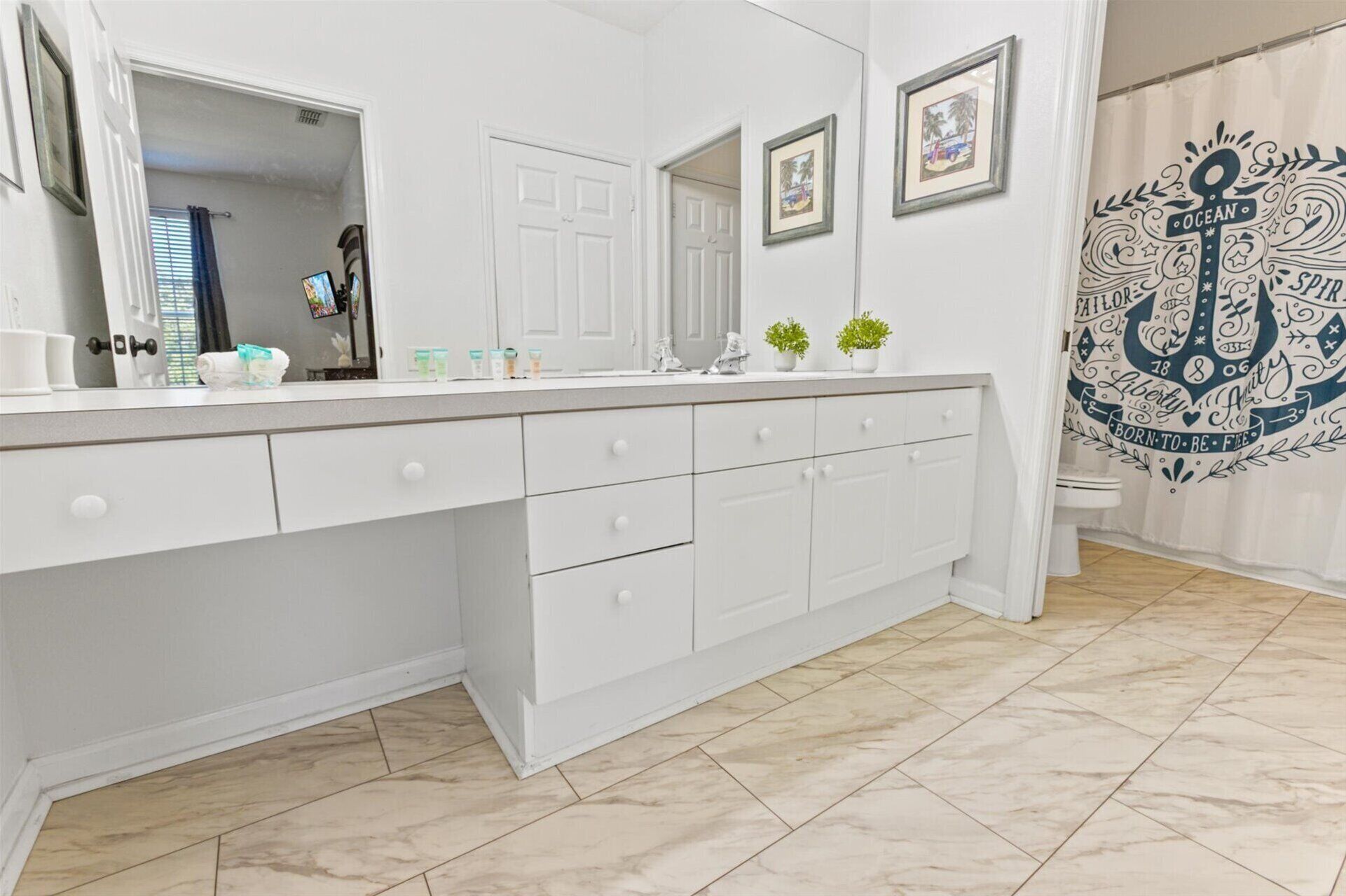 A bathroom with a large mirror, white cabinets, and a tiled floor.