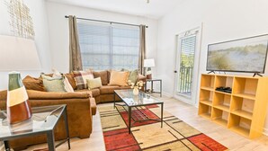 A living room with a brown leather sofa, a glass coffee table, a TV on a wooden stand, and a patterned rug.