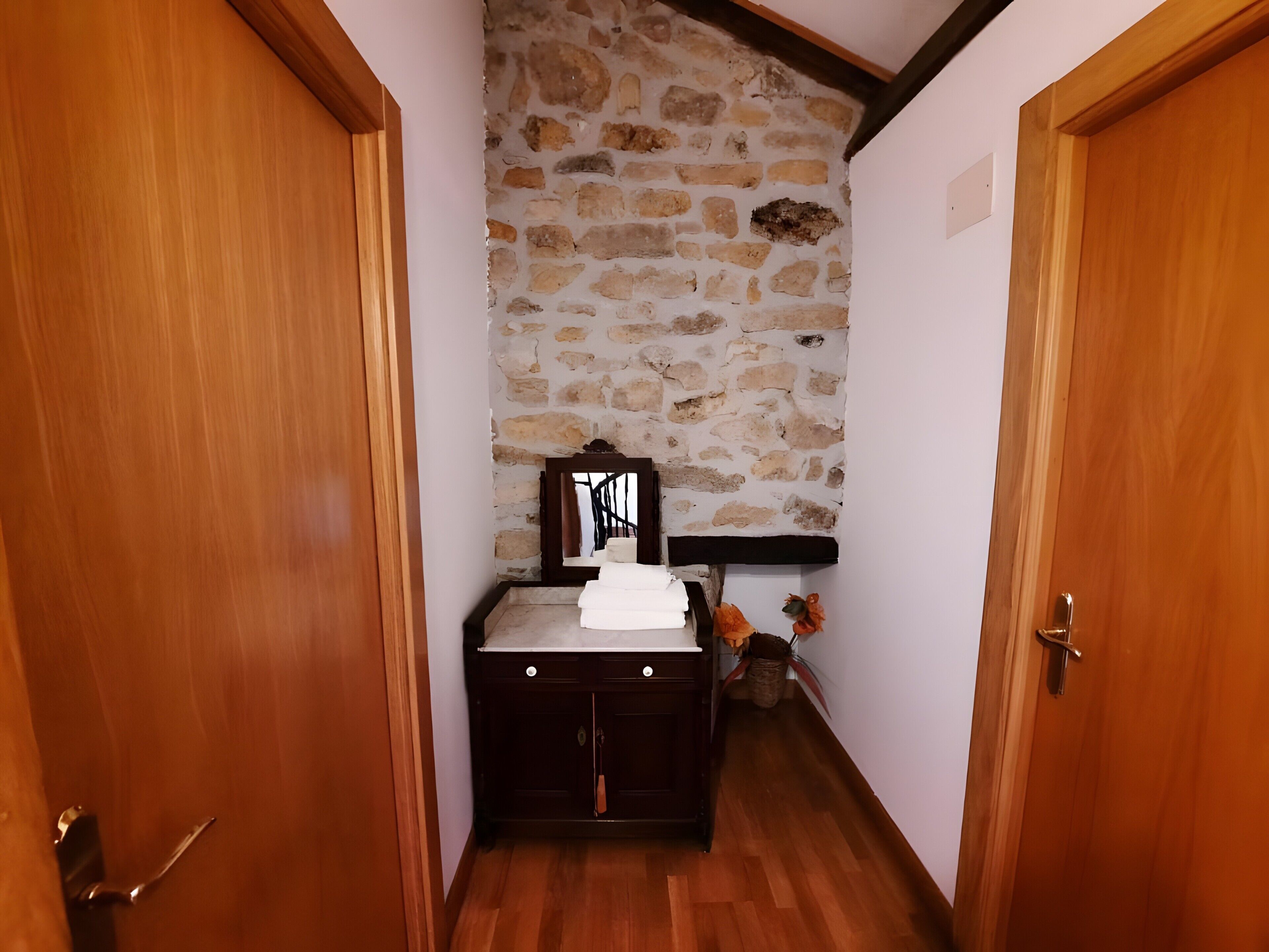 Un couloir avec un mur en pierre, des portes en bois et une petite armoire dotée d’un miroir.