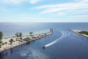 A coastal area with a jet ski on a calm waterway, a beach with palm trees, and a rocky breakwater.