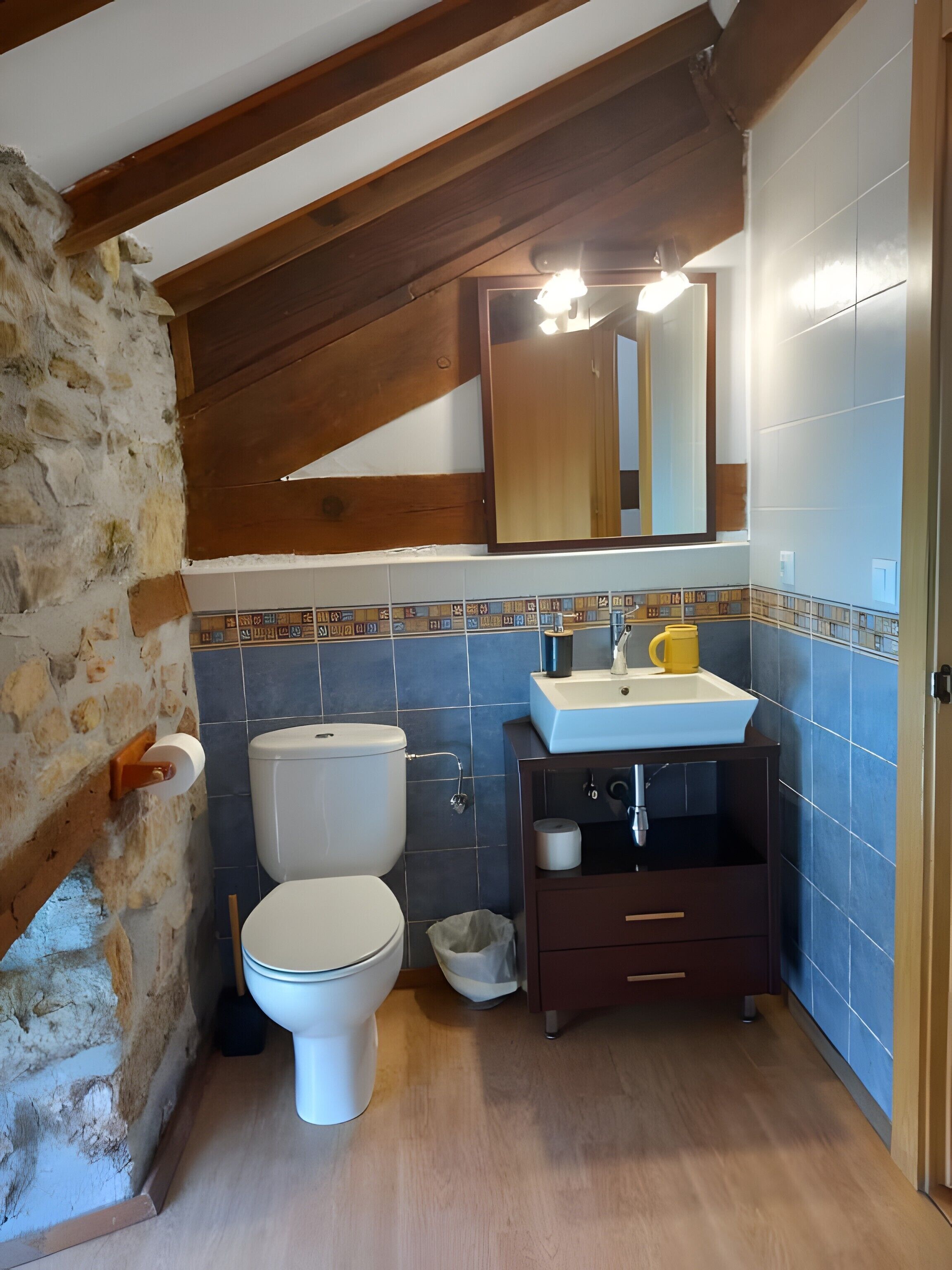 Un baño con inodoro, lavabo, espejo y vigas de madera.