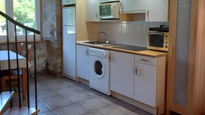 A compact kitchen with a washing machine, microwave, and oven, wooden beams on the ceiling, and a dining area with a table and chairs. - Apartment in Alsasua with Shared Pool, Wi-Fi and Air Conditioning (Alsasua)