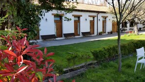 A white building with wooden doors and windows, benches along the pathway, and a well-maintained lawn. - Apartment in Alsasua with Shared Pool, Wi-Fi and Air Conditioning (Alsasua)