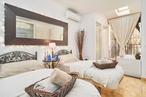 A hotel room with two beds, a large mirror, bedside lamps, a small table, and a window with curtains.