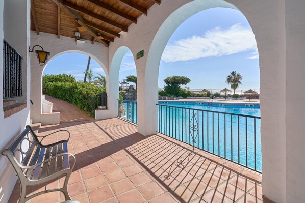 A covered outdoor area with a bench, a pool, and a view of the surrounding landscape.