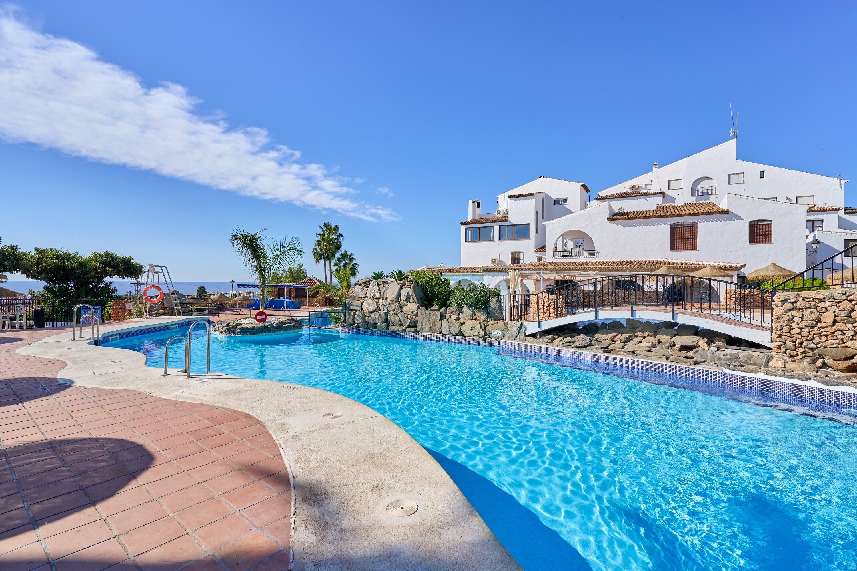 A swimming pool with a stone wall and a white building with multiple balconies in the background.