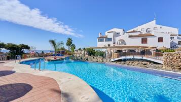 A swimming pool with a stone wall and a white building with multiple balconies in the background.