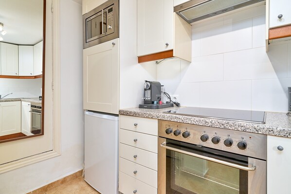 A kitchen with white cabinetry, a built-in oven, a coffee maker, and a microwave.