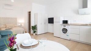 A modern hotel room with a bed, a dining table with plates and glasses, a washing machine, and a microwave. - Studio Apartment 'Apartamentos Maria' with Wi-Fi and Air Conditioning (Vejer de la Frontera)