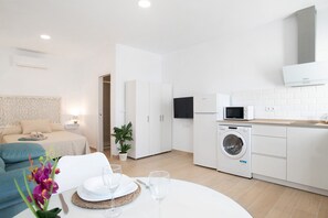 Ett modernt hotellrum med en säng, ett matbord med tallrikar och glas, en tvättmaskin och en mikrovågsugn.