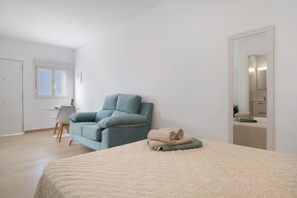 A bedroom with a bed, a chair, a desk, and a mirror.