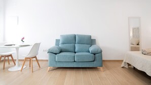 A modern living room with a blue sofa, a small round table with chairs, a bed with a white bedspread, and a large mirror on the wall. - Studio Apartment 'Apartamentos Maria' with Wi-Fi and Air Conditioning (Vejer de la Frontera)
